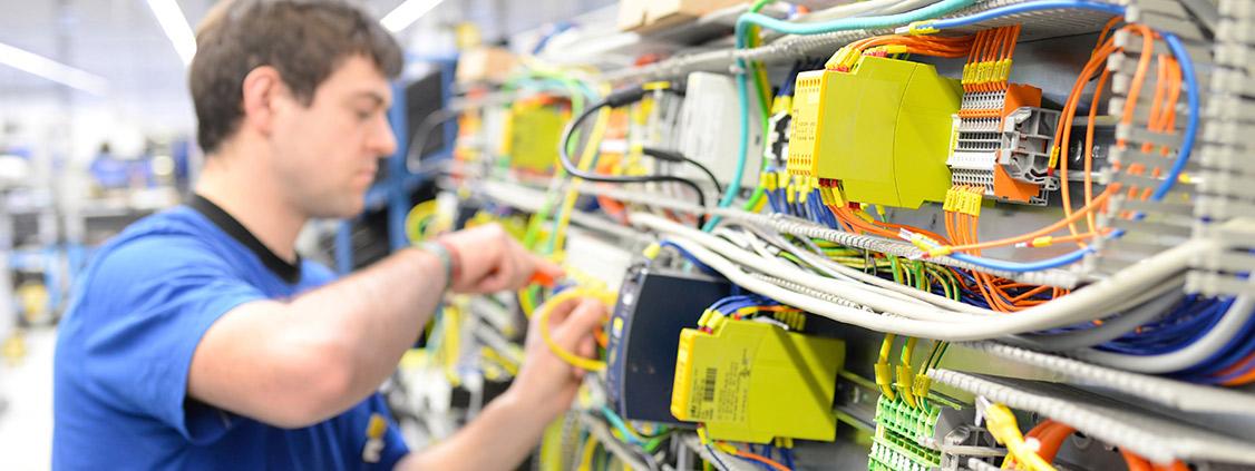 UNIS Group technician wiring and testing components in an industrial electrical control cabinet.